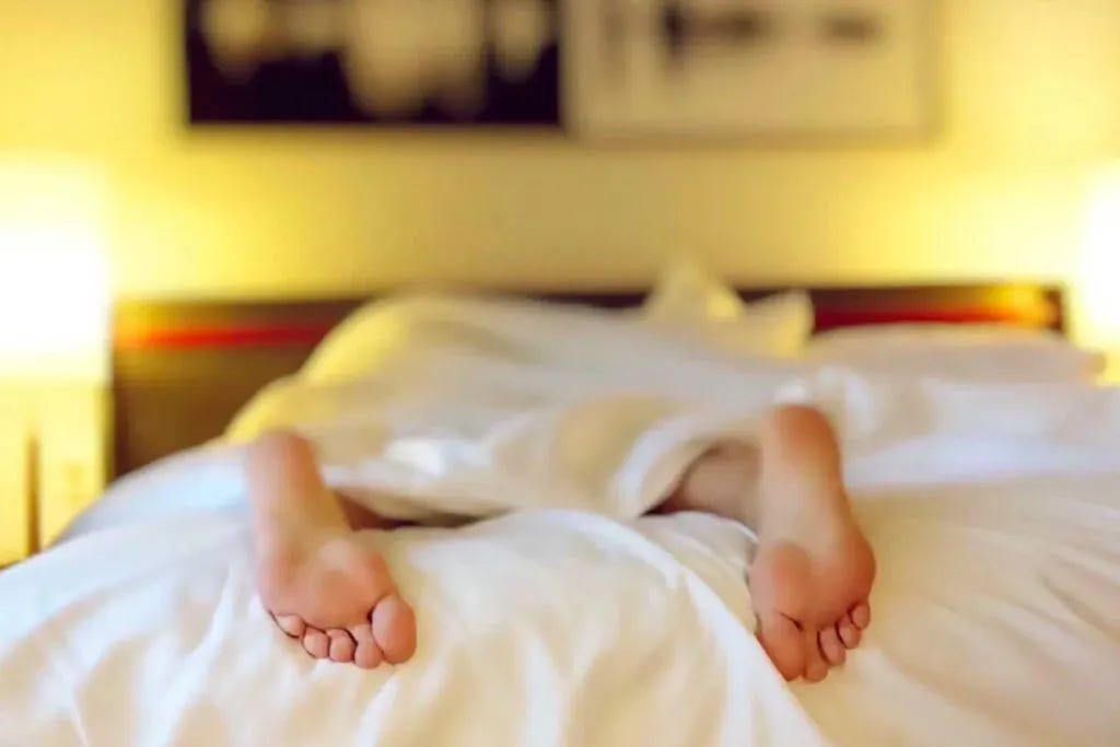 Feet hanging out from covers in a hotel bed.